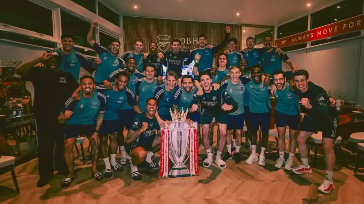 Pemain Arsenal merayakan kemenangan dengan mengangkat trofi Premier League di tengah lapangan, suporter bersor