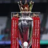 Trofi Premier League dari perak murni berkilau dengan latar belakang pita merah dan putih khas Arsenal