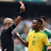 Wasit sedang mengangkat kartu merah di hadapan pemain yang sedang tertunduk lesu di lapangan hijau