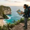 Ilustrasi backpacker dengan ransel besar berdiri di tepi pantai sambil memegang peta dan melihat pemandangan